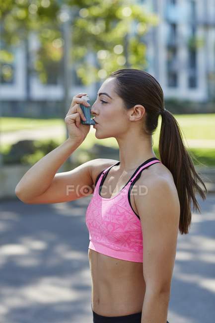 Mujer joven en ropa deportiva usando inhalador . - foto de stock