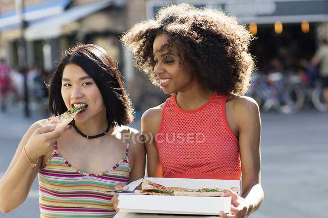 Dos mujeres jóvenes comiendo pizza de la caja . - foto de stock