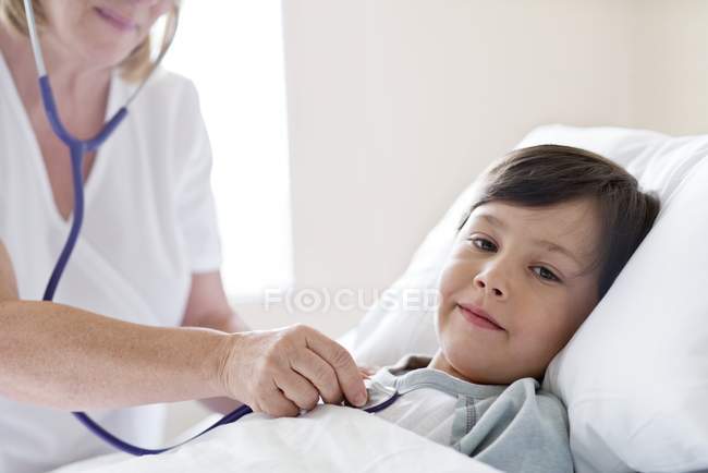 Медсестра використовує стетоскоп на хлопчика в лікарняному ліжку . — стокове фото