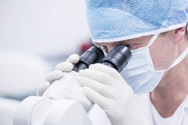 Científico masculino en máscara protectora usando microscopio . - foto de stock