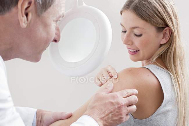 Medico maschio che esamina la talpa del paziente con dermatoscopio . — Foto stock
