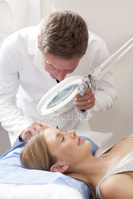 Médico masculino examinando jovem mulher usando lâmpada de ampliação
. — Fotografia de Stock