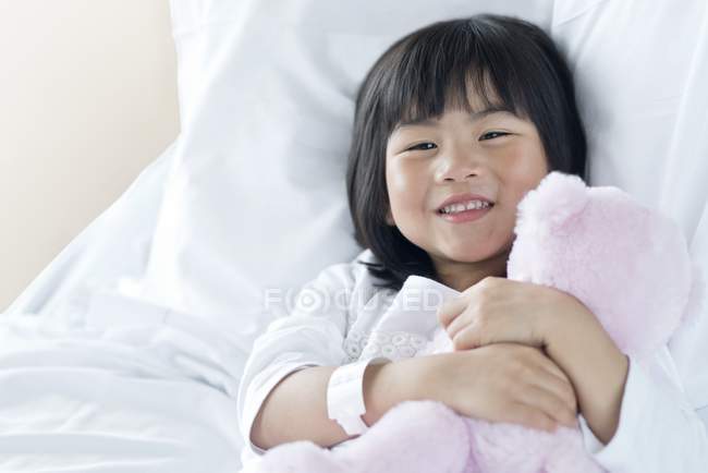 Menina asiática na cama do hospital com ursinho de pelúcia . — Fotografia de Stock