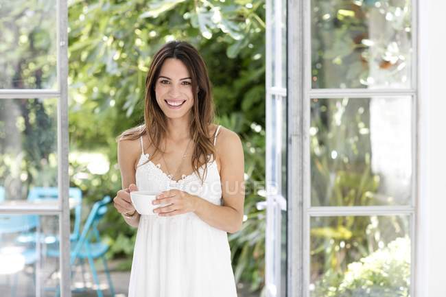 Woman standing in doorway holding coffee cup. — Stock Photo