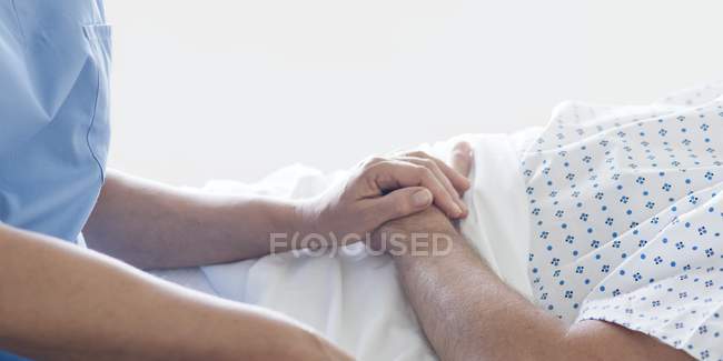 Infermiera femminile che tiene la mano del paziente maschio nel letto d'ospedale . — Foto stock