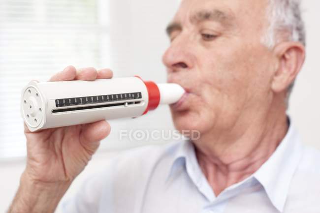 Hombre mayor exhalando en el lector de flujo máximo . - foto de stock