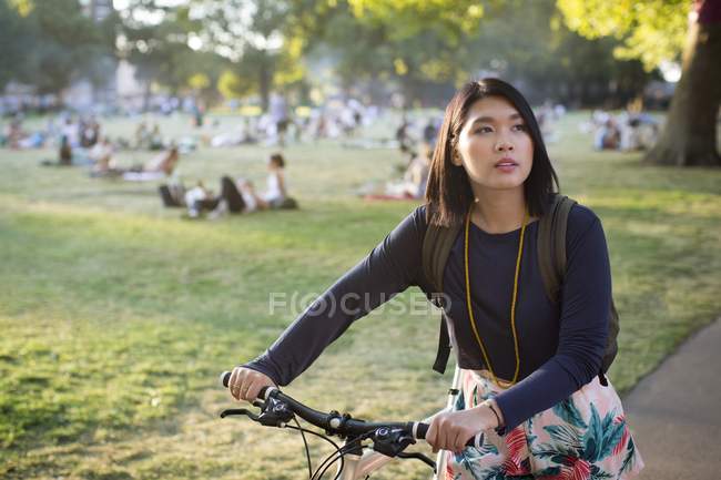 Asian woman pushing bicycle in park. — Stock Photo