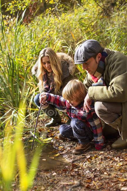 Familie hockt am Teich und schaut ins Wasser. — Stockfoto