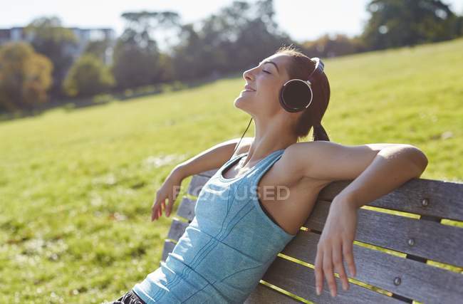 Junge Frau hört Musik, während sie auf Bank sitzt. — Stockfoto
