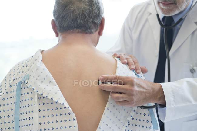 Male doctor examining patient in hospital gown. — Stock Photo