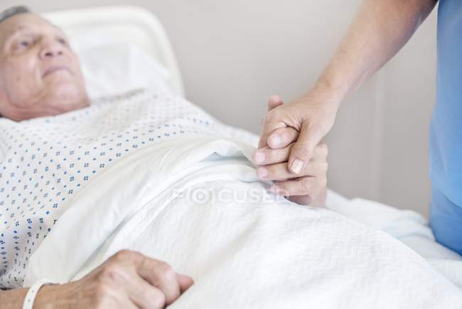 Female nurse holding senior patient hand in hospital bed. — Stock Photo