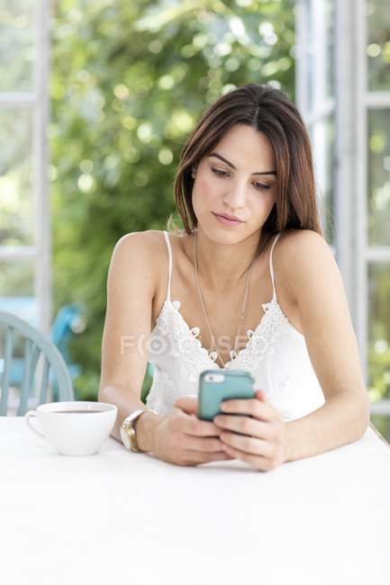 Молода жінка використовує смартфон за столом . — стокове фото