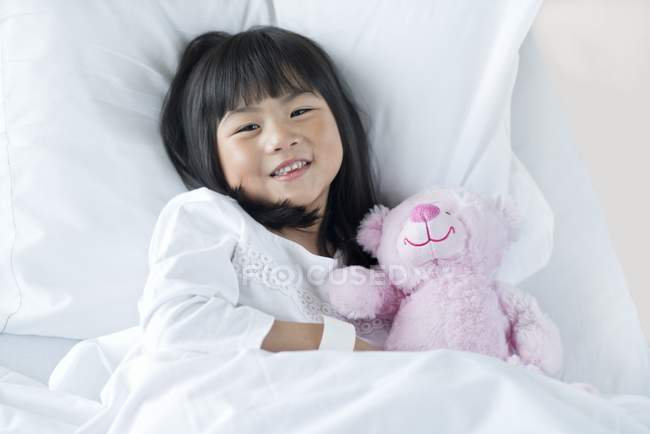 Asiatin liegt mit Teddybär im Krankenhausbett. — Stockfoto