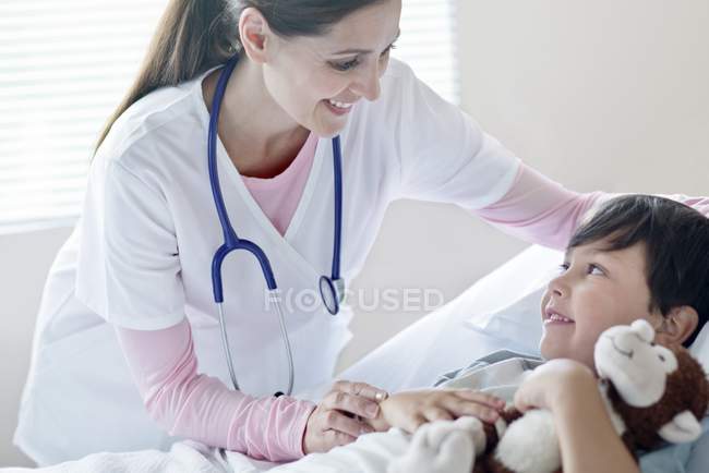 Хлопчик в лікарняному ліжку зі усміхненою жінкою-медсестрою . — стокове фото