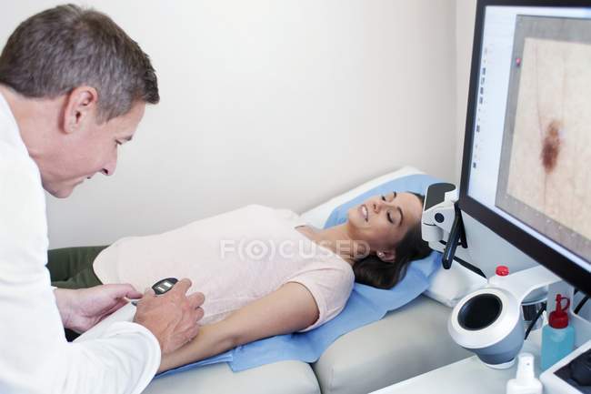Médico masculino examinando lunar en brazo de paciente femenino . - foto de stock