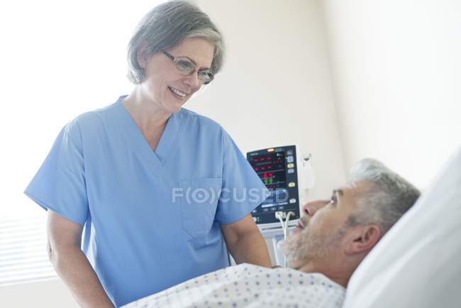 Enfermeira mulher conversando com paciente do sexo masculino na cama do hospital . — Fotografia de Stock