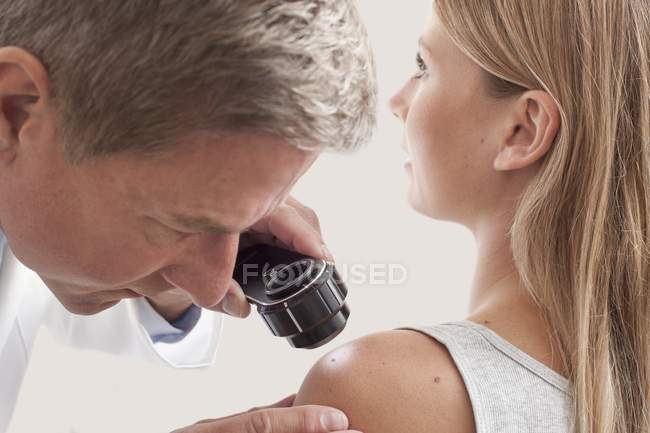 Médico masculino examinando a toupeira do paciente com dermatoscópio . — Fotografia de Stock