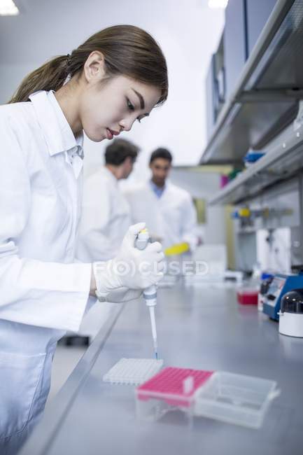 Female scientist working in laboratory with colleagues in background. — Stock Photo