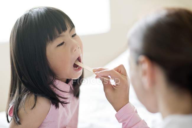 Female nurse using tongue depressor on asian girl. — Stock Photo