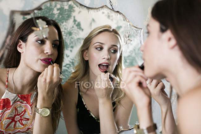Junge Frauen tragen Lippenstift im Spiegel auf. — Stockfoto
