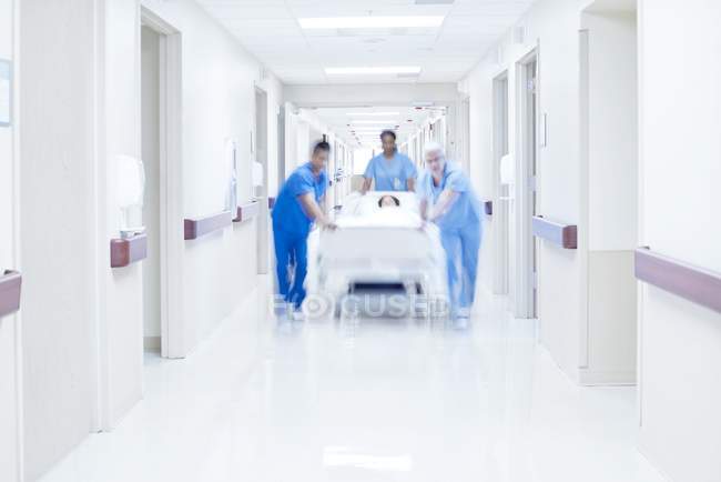 Ärzte schieben Krankenhausbett mit Patient durch Flur. — Stockfoto