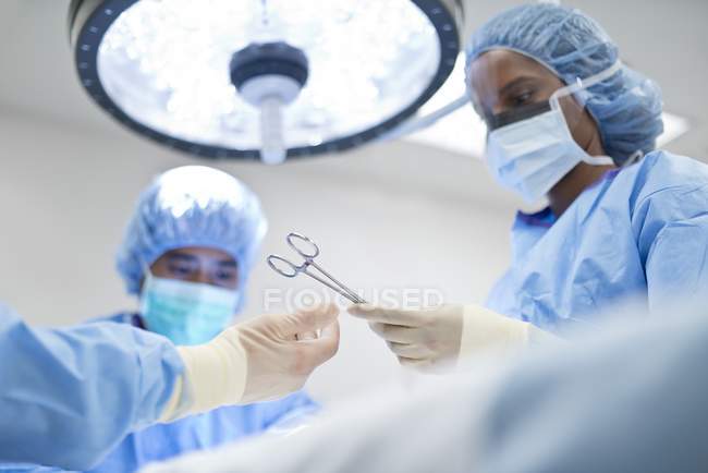 Enfermera pasando tijeras quirúrgicas al cirujano durante la operación . - foto de stock