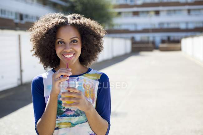 Mulher sorridente com bebida em pé na rua . — Fotografia de Stock