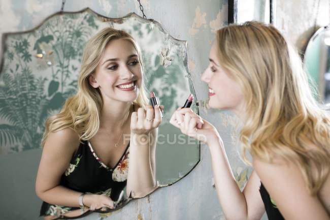 Jovem mulher aplicando batom no espelho. — Fotografia de Stock