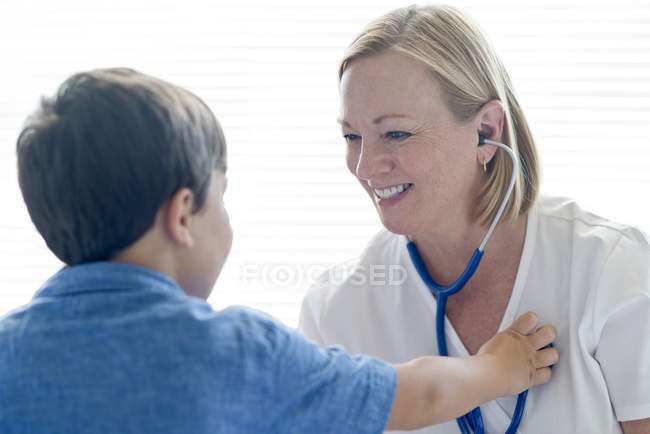 Усміхнена медсестра зі стетоскопом сидить з хлопчиком . — стокове фото