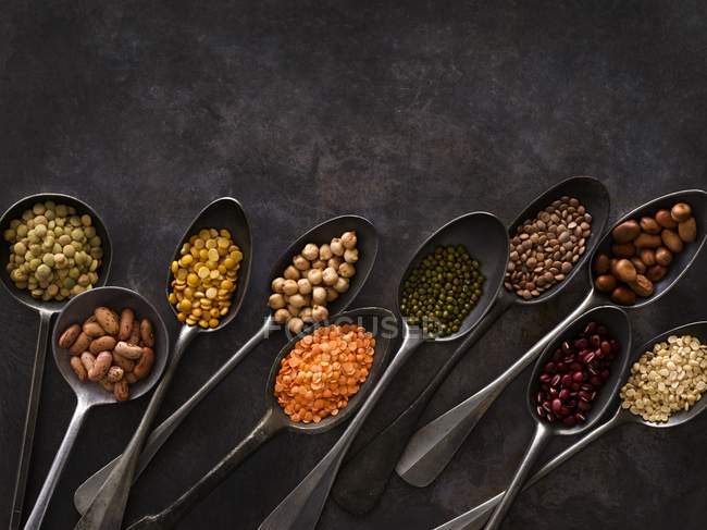 Various pulses in metal spoons on black background. — Stock Photo