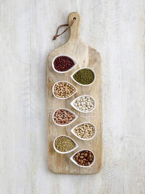 Legumes in tear shaped mini bowls on chopping board, overhead view. — Stock Photo