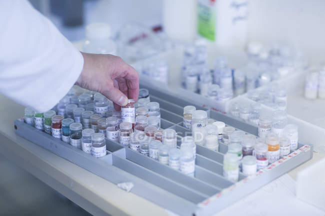 Chemist hand picking samples stored in crimp neck vials in pharmaceutical laboratory. — Stock Photo