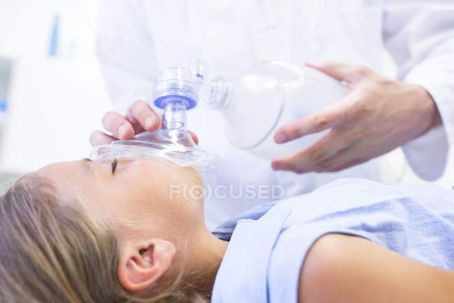 Close-up of hands of male doctor putting anaesthetic mask on girl. — Stock Photo