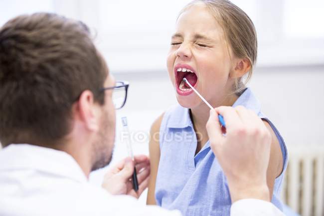 Médico tomando muestra de hisopo de la boca chica joven
. - foto de stock