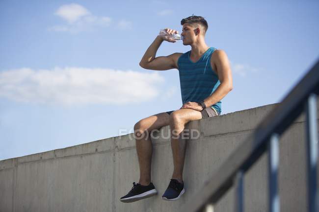 Mann sitzt auf Dach und trinkt Wasser aus Flasche. — Stockfoto