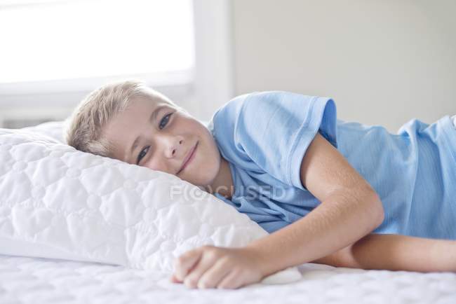 Хлопчик лежить з головою на подушці і посміхається . — стокове фото