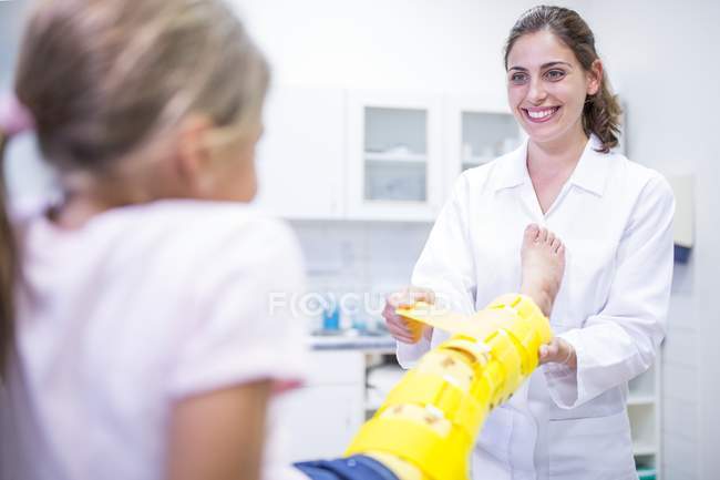 Medico mettendo tutore gamba gialla sulla ragazza . — Foto stock