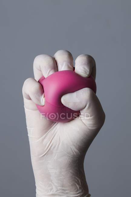 Guante de mano en látex que sostiene la bola de estrés . - foto de stock