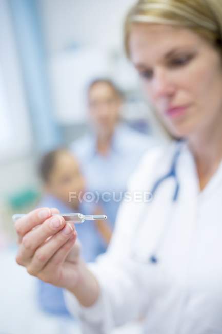 Doctor looking at thermometer with people in background. — Stock Photo