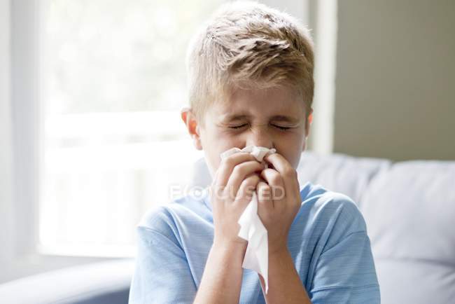 Preteen boy blowing nose indoors. — Stock Photo