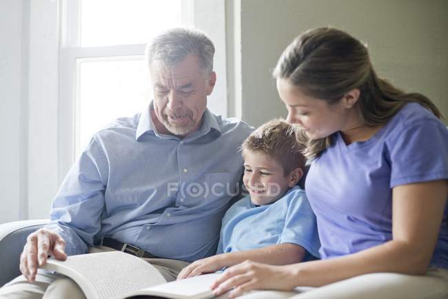 Nonno, madre e figlio leggono insieme il libro . — Foto stock