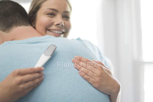 Mujer abrazando hombre y sosteniendo prueba de embarazo . - foto de stock