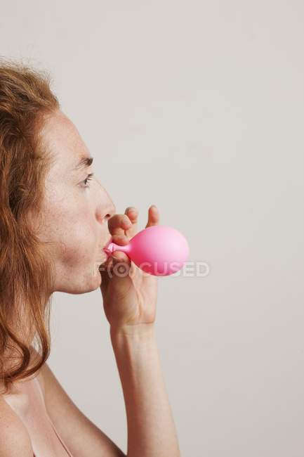 Profil einer jungen Frau mit roten Haaren, die einen rosa Luftballon in die Luft sprengt. — Stockfoto