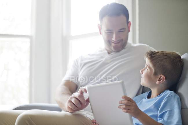 Garçon utilisant une tablette numérique avec père à l'intérieur . — Photo de stock