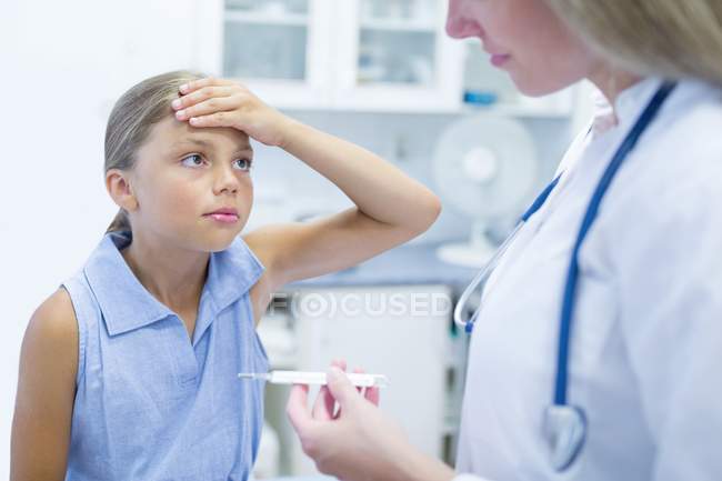 Menina com a mão na testa olhando para o médico feminino com termômetro . — Fotografia de Stock