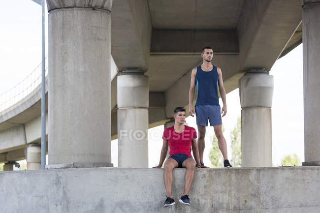 Atletas masculinos descansando sob ponte de concreto . — Fotografia de Stock