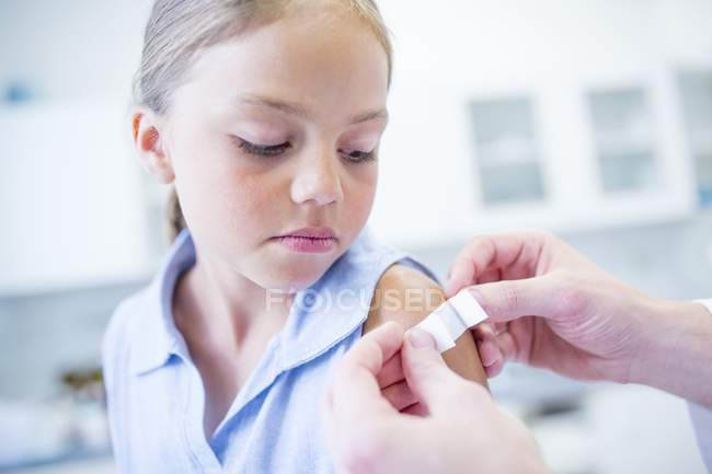 Person applying plaster to young girl shoulder — Stock Photo