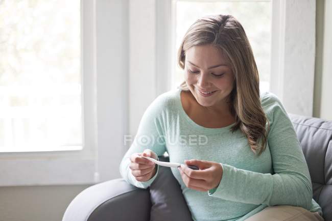 Frau sitzt auf Sofa und schaut auf Schwangerschaftstest herunter. — Stockfoto