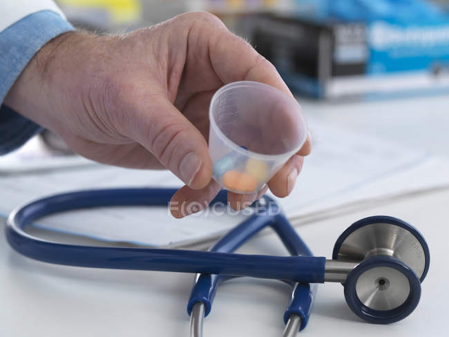 Arzt hält Plastikbecher mit Medikamenten. — Stockfoto