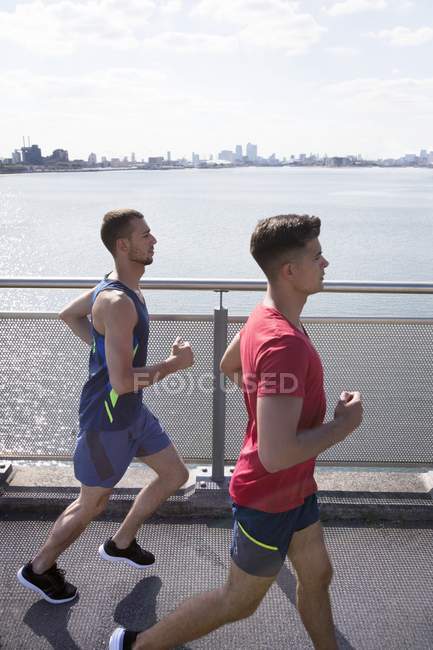 Atletas do sexo masculino correndo na margem do rio . — Fotografia de Stock